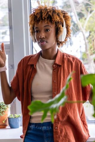 African american woman wearing headphones standing by window observing indoor plants