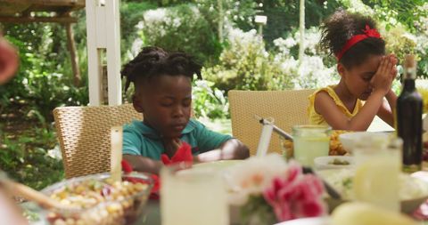 Diverse brother and sister saying grace at family dinner table in sunny garden - Download Free Stock Photos Pikwizard.com