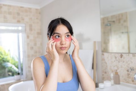 Young asian woman applying pink under-eye hydrogel patches during morning skincare routine