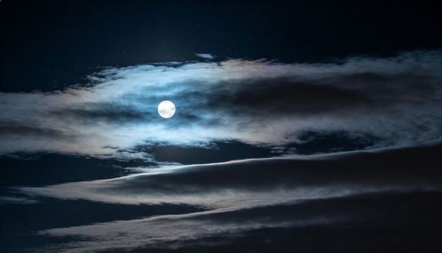 Full Moon Casting Silk-like Halo Over Layered Clouds and Deep Starry Night Sky