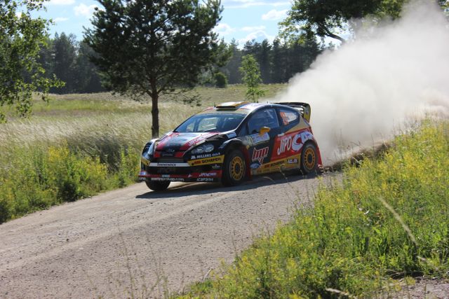 Rally car speeding on a dusty gravel road in countryside; suitable for content related to motorsport, automotive, outdoor adventure, speed, competition events advertising, racing blogs, action sports marketing.