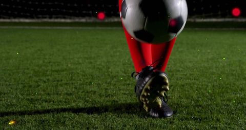 Closeup of soccer player kicking ball on night turf with red socks black cleats