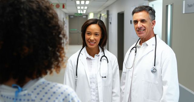 A diverse group of medical professionals, including an Asian and a Caucasian, are engaging with a patient in a hospital corridor, with copy space. Their friendly demeanor suggests a positive interaction, discussing healthcare options or providing medical advice.