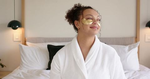 African american woman relaxing in white bathrobe wearing gold under-eye patches