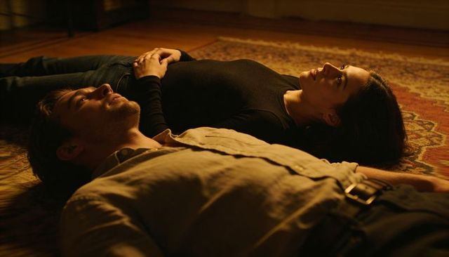 Couple lying on rug staring at ceiling in warm lamplight, intimate casual moment