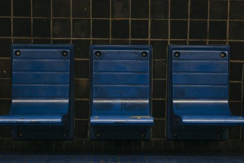 Three blue plastic seats against black tiled wall in row