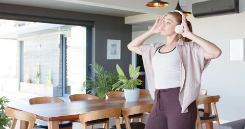 Relaxing woman enjoying music with over-ear headphones in modern sunlit dining room scene