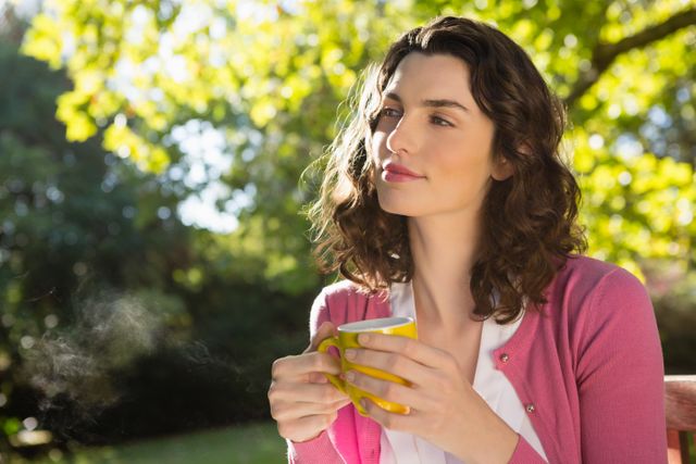 Thoughtful woman holding a cup of coffee in garden
