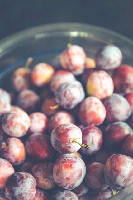 Shows fresh ripe plums in a glass bowl, emphasizing the fruit's vibrant color and texture. Ideal for health food blogs, culinary websites, or marketing materials related to fruit consumption and organic food.