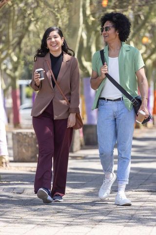 Friends walking and chatting on tree-lined city path holding takeaway coffee cups