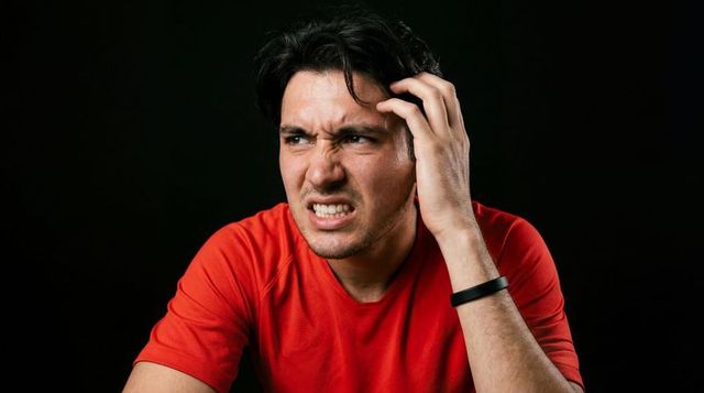 Hispanic man clutching temple grimacing closeup in red shirt with black wristband