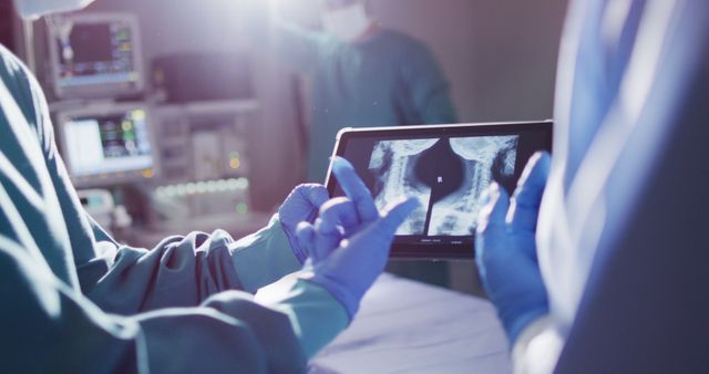 Image of midsection of two gloved surgeons discussing x-ray on tablet in operating theatre. Hospital, medical and healthcare services.