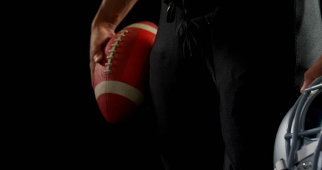 An American football player holding a football in one hand and a helmet in the other, against a dark background. The image captures the intensity and focus of the player, making it suitable for sports-related content, athlete promotion, team sports posters, and competitive spirit themes. It is perfect for use in advertising, marketing materials, and social media posts related to American football.