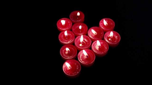 Red candles arranged in a heart shape are flickering in the dark. This makes it suitable for use in themes around romance, valentine's day, meditation, peaceful environments, or nighttime celebrations. It can also be used in blogs or articles discussing romance, tranquility, or tips for creating a cozy atmosphere.