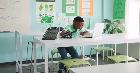 Young Black student studying renewable energy with solar panel and wind models in STEM lab
