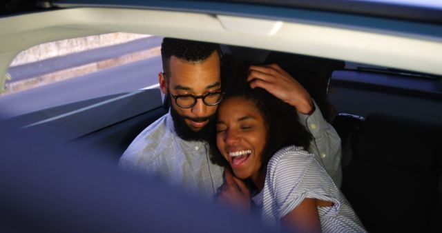 Romantic diverse couple smiling and embracing on car in city street at night. City living, transport, romance, love, relationship, free time and lifestyle, unaltered.