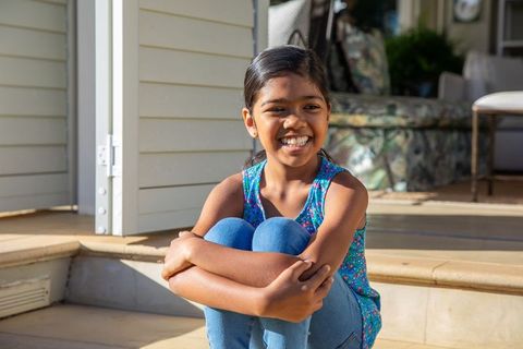 Happy Asian Girl Sitting on Porch Steps in Sunshine