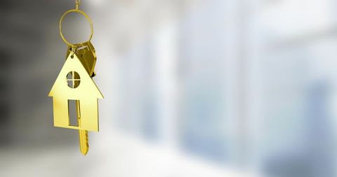 Gold house keyring hanging in bright interior representing home ownership and real estate