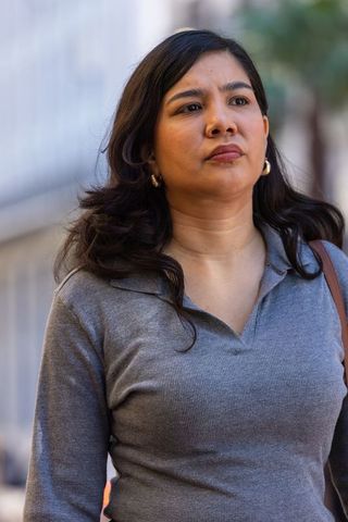 Thoughtful woman walking on city sidewalk wearing grey collared top and hoop earrings