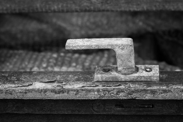 Close-up of a rusty metal door handle displayed in black and white, showcasing the aged and worn texture. The image emphasizes the handle's deterioration and vintage feel. Suitable for themes such as decay, time, history, or industrial aesthetics. Ideal for use in artistic projects, vintage or antique-themed designs, and industrial-related presentations or websites.