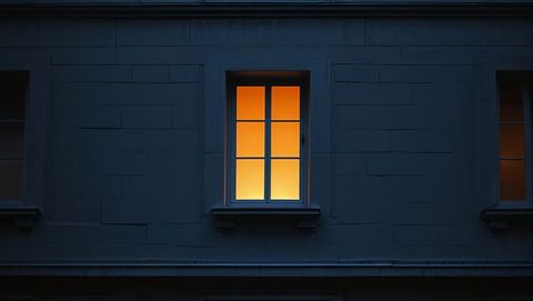Warm light through muntined window on dark exterior wall at night