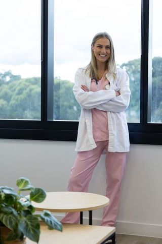 Smiling female clinician standing by window in bright clinic wearing pink scrubs