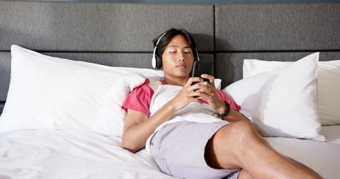 Teen Relaxing with Headphones and Smartphone on Bed