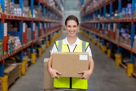 Smiling Warehouse Worker Holding Cardboard Box in Aisle