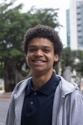Smiling young man standing on urban sidewalk wearing navy polo and gray zip-up hoodie