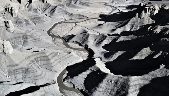 Meandering muddy river carving layered badlands from aerial view, arid canyon landscape