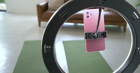 Ring light holding pink smartphone over yoga mat for recording home workout and streaming