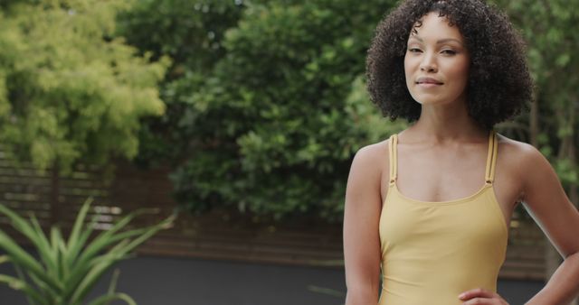 Portrait of biracial woman wearing swimsuit in sunny garden with copy space. Lifestyle, free time, nature and domestic life, unaltered.