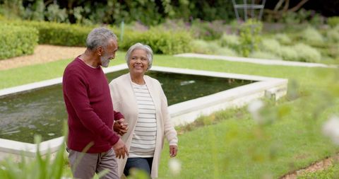 Smiling Senior Couple Walking Hand in Hand in Serene Garden