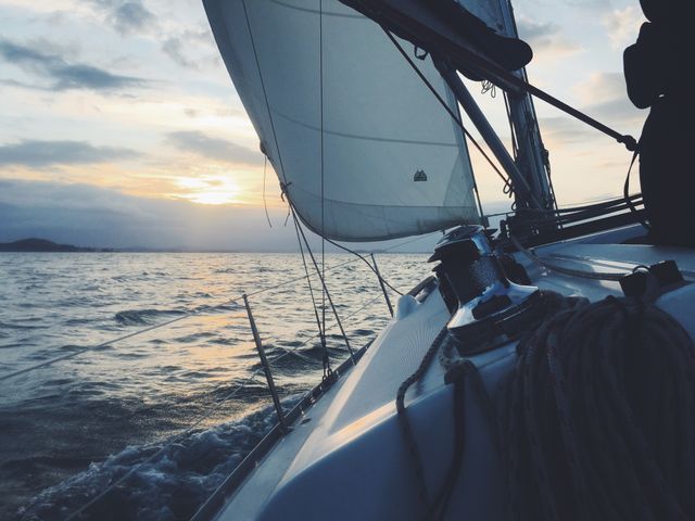 Sailboat gliding on ocean with dramatic sunset sky. Great for travel blogs, sailing magazines, marine equipment promotions, or relaxation themes. Adds serene and adventurous elements to websites and marketing materials.