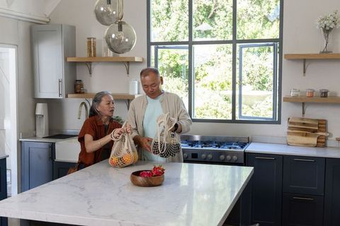 Senior couple unpacking reusable mesh produce bags on sunlit modern marble kitchen island
