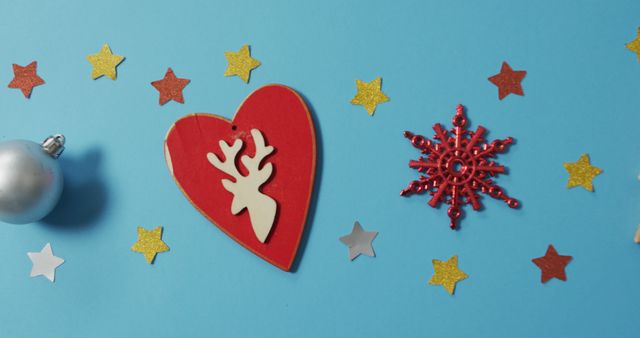 Christmas-themed decorations including a red heart with a reindeer, silver and gold stars, and a red snowflake ornament placed on a bright blue background. Ideal for holiday greetings, festive promotions, seasonal advertisements, or Christmas-themed designs and crafts.