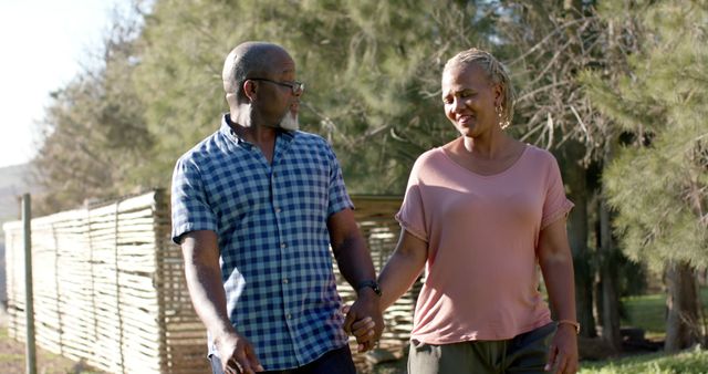 Happy senior african american couple holding hands walking and talking in sunny garden. Retirement, fitness, wellbeing, summer and active senior lifestyle, unaltered.