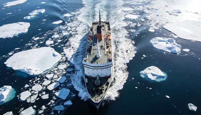 Icebreaker cutting through arctic ice floes from aerial view showing bow wake and deck