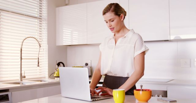 Woman using laptop while having breakfast in kitchen at home 4k