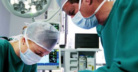 Surgeon and Assistant Performing Surgery in Operating Room with Surgical Lights and Monitors