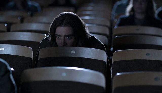 Man peering over seat in dim auditorium, creating suspenseful cinematic mood and isolation