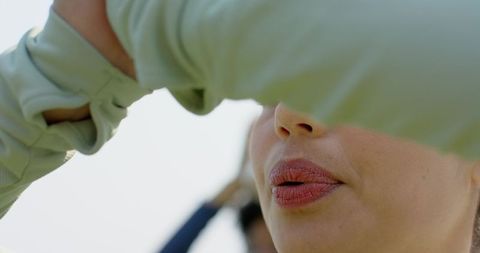 Woman shielding eyes with thumbhole sleeve while talking outdoors, sunlit lips closeup