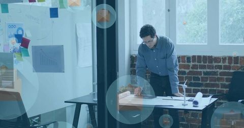 Architect reviewing blueprints in modern loft office with natural light leaning over desk