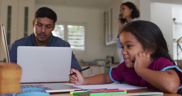 Hispanic girl sitting at table drawing with parents working in background - Download Free Stock Photos Pikwizard.com