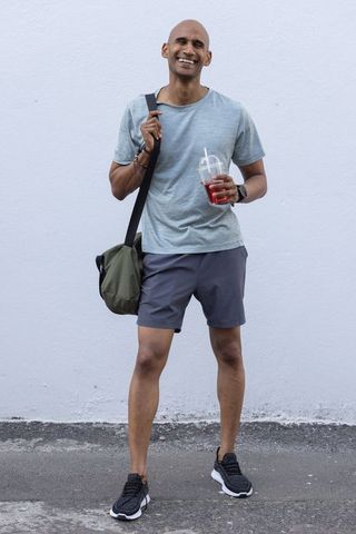 Smiling african man with duffel bag sipping cold drink, casual urban active lifestyle