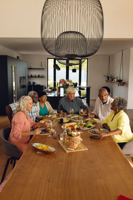 Multiracial senior friends talking and having lunch while sitting at dining table in nursing home. Copy space, unaltered, meal, alcohol, togetherness, support, assisted living and retirement.