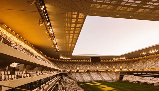 Modern open-roof stadium interior golden hour showing geometric tiers and retractable roof