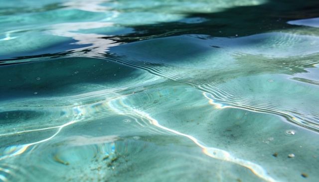 Turquoise water rippling and shimmering with sun caustics over sandy bottom closeup