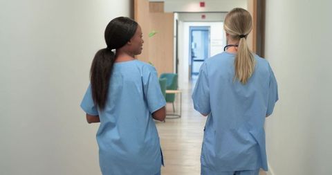 Diverse nurses walking and talking in clinic corridor wearing blue scrubs