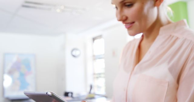 This photo of a woman using a smartphone in a modern office setting can be used for articles, blog posts, websites, or advertisements related to business, technology, communication, work-life balance, or professional settings. It conveys a sense of modern work culture and productivity.